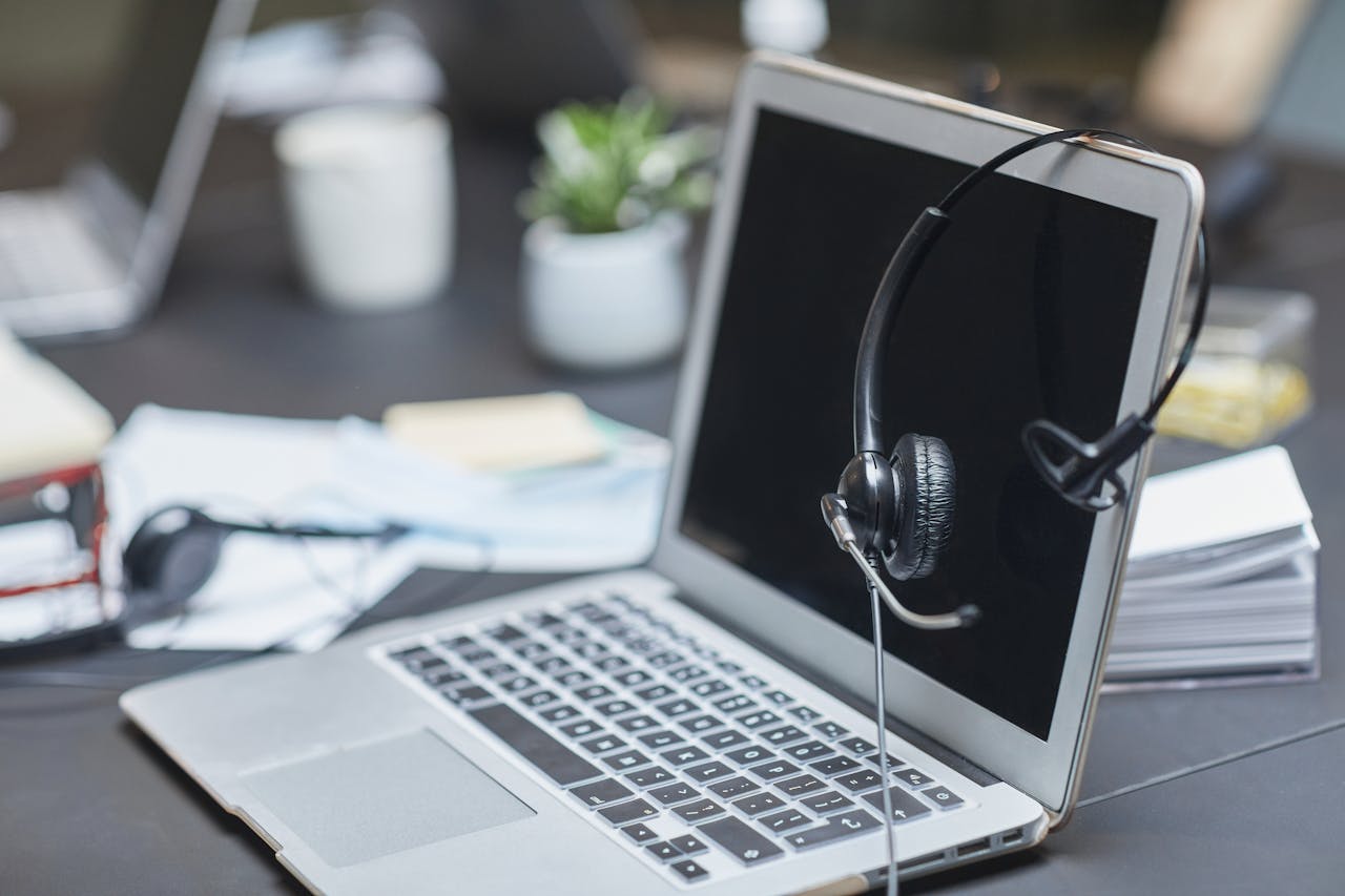 A headset placed on a laptop in a modern, cluttered office setting with papers and plants.